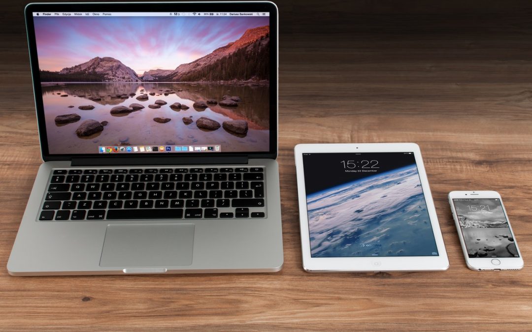 Image of multiple apple products placed on top of desk. Iphone, ipad and macbook.